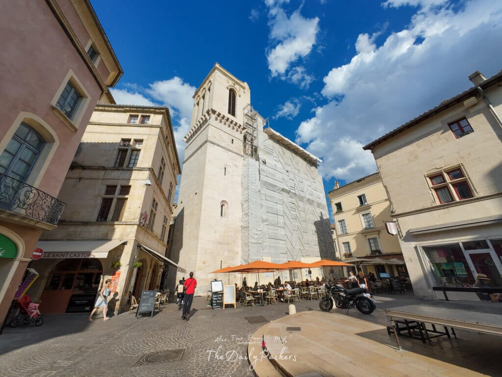 Vue sur la cathédrale de Nîmes entourée de bâtiments charmants et d'un café en terrasse