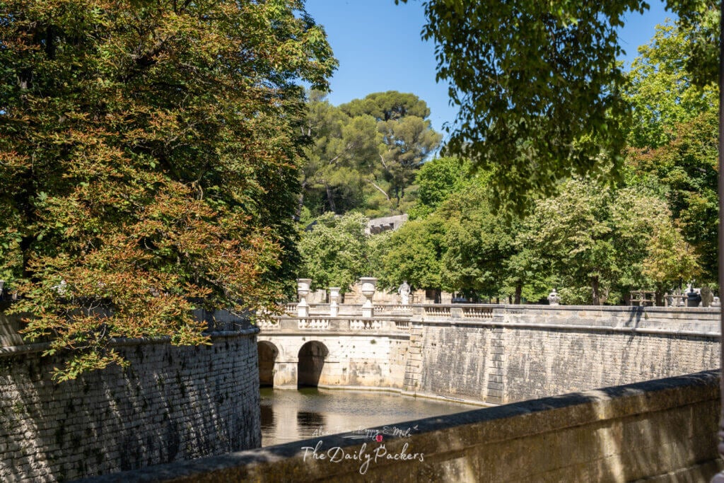 Canal calme bordé d'arbres avec des ponts en pierre et un charme historique au cœur de Nîmes