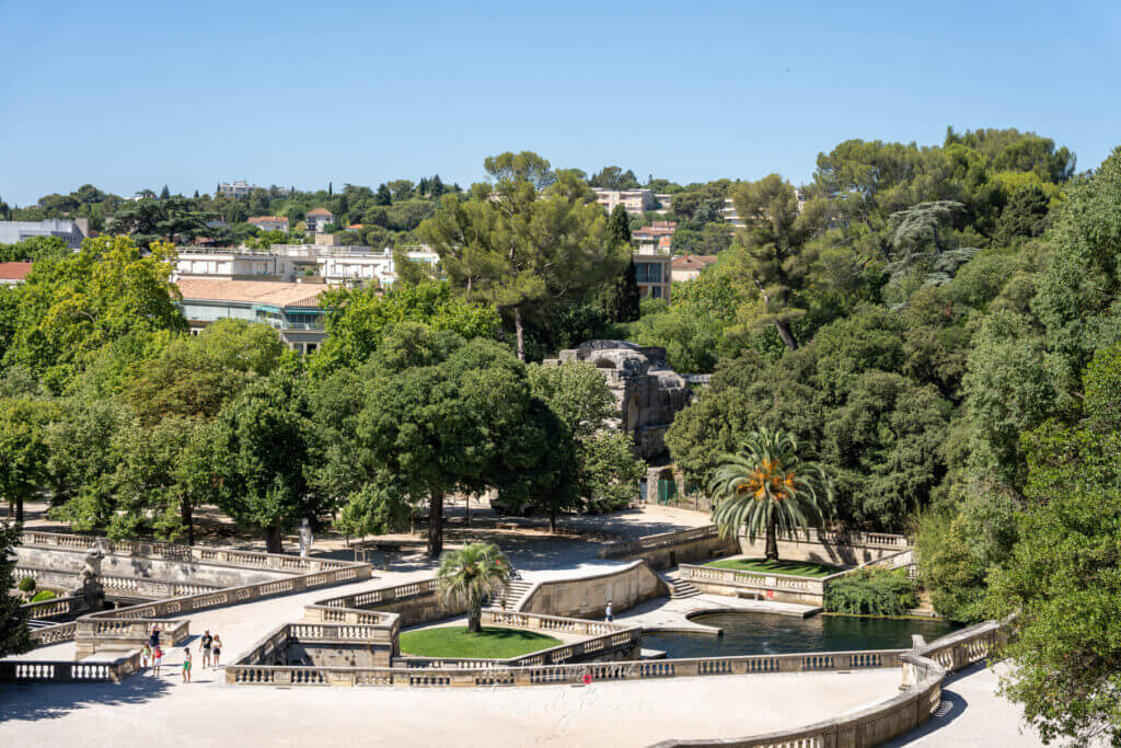 Vue aérienne du Jardin de la Fontaine à Nîmes, montrant les allées bordées d'arbres, les bassins et le temple de Diane au loin.