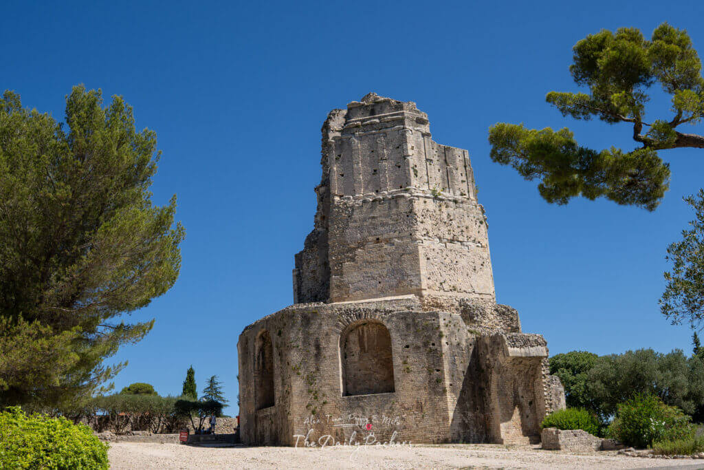 Vue de l'ancienne tour romaine Tour Magne à Nîmes sous un ciel bleu lumineux, entourée d'arbres.