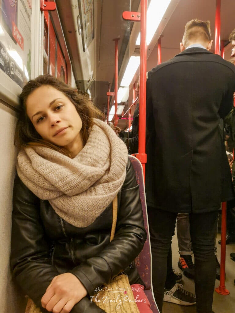 Tired commuter resting against the wall inside a busy Prague metro train, surrounded by standing passengers.