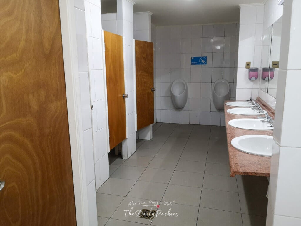 Men’s restroom at Refugio Grey with urinals, sinks, and toilet cubicles.