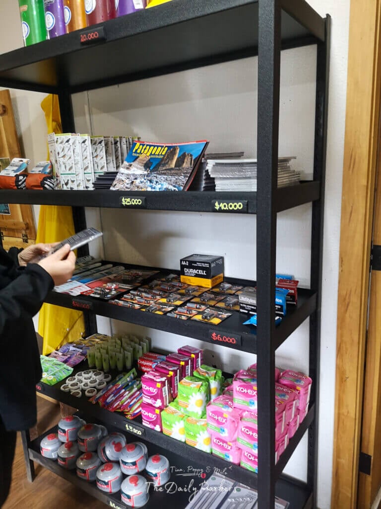 Shelves with camping supplies, toiletries, books, and gas canisters for sale inside the Refugio Grey shop.