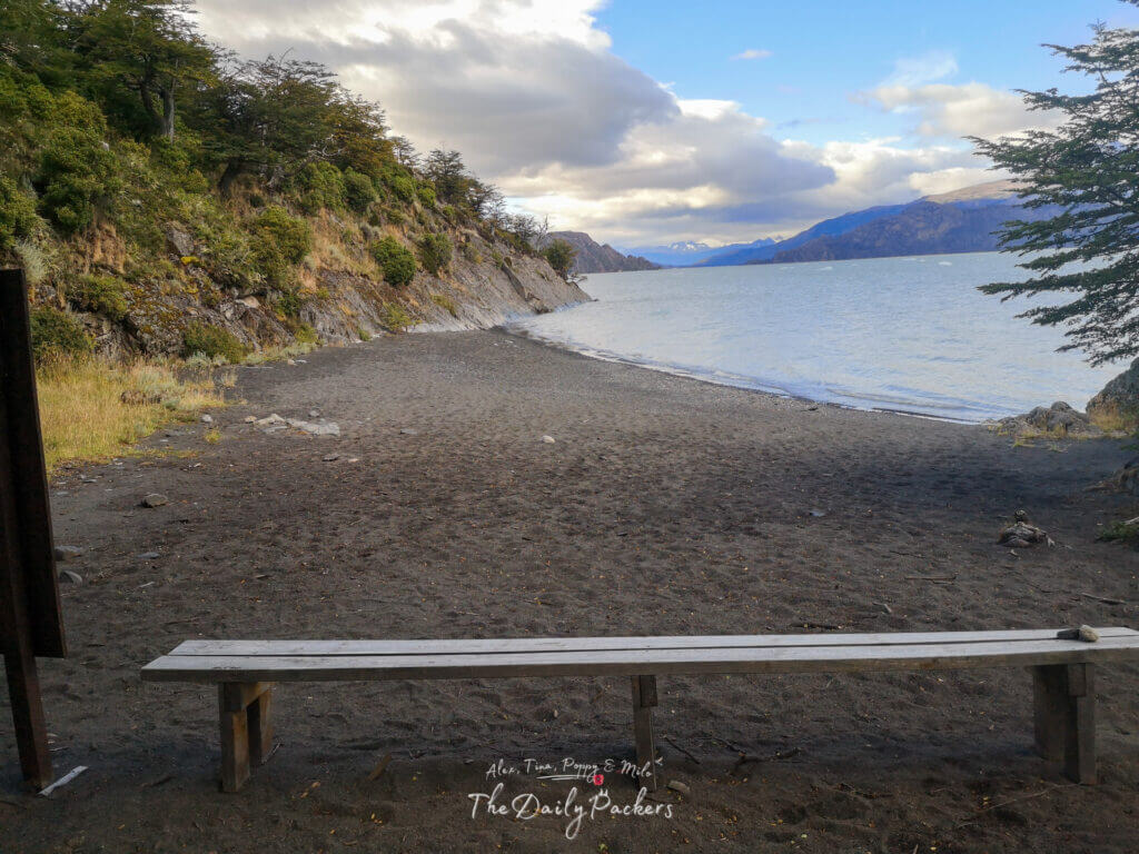 Small black sand beach along the shore of Lago Grey in Torres del Paine with a simple wooden bench.