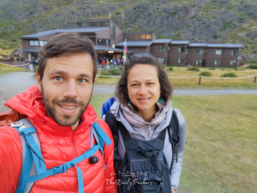 Couple standing in front of Refugio Paine Grande, dressed in hiking gear and ready for the day’s trek.