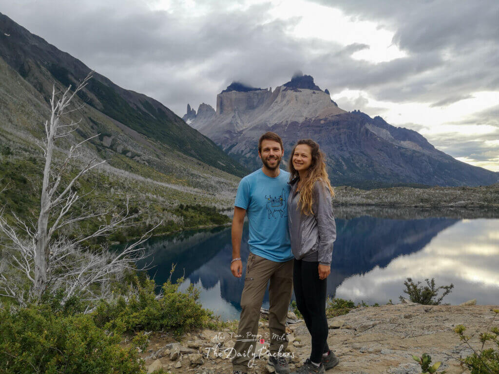 Couple smiling together with Cuernos del Paine and its perfect lake reflection in the background in Torres del Paine.