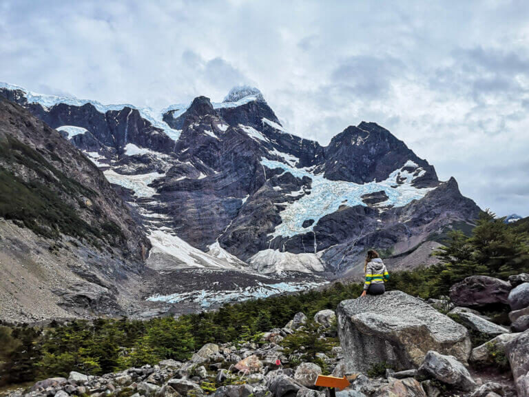 Hiker sitting on a rock admiring the dramatic glacier-covered peaks of Mirador Francés in Torres del Paine National Park during the W-Trek Day 3
