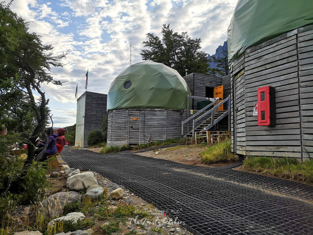 Groupe d'éco-cabines à dôme vert avec des extérieurs en bois à Domos Frances sous un ciel partiellement nuageux.