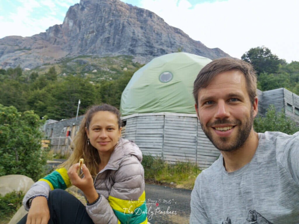 Couple smiling in front of Domos Frances with towering rocky cliffs in the background in Torres del Paine.
