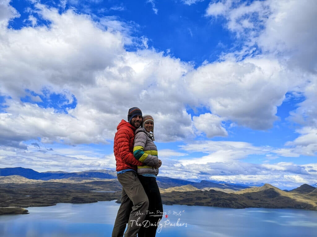 Couple in colorful jackets smiling and posing together on a high viewpoint with sweeping views of lakes and mountains in Torres del Paine.