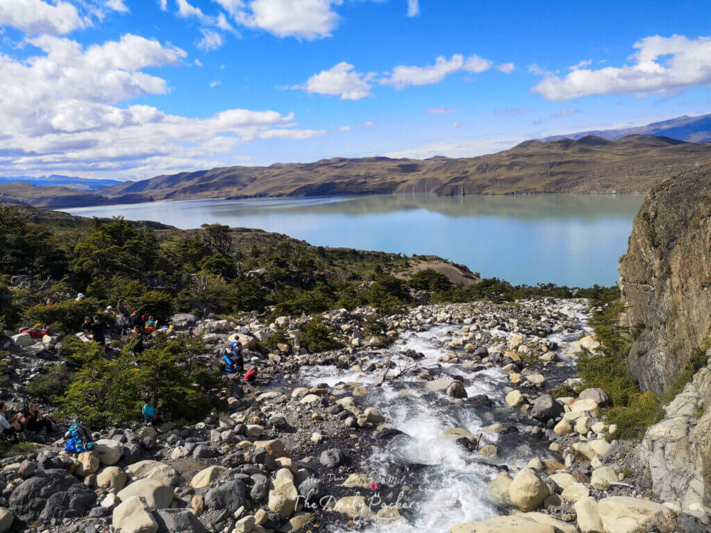Rocky river cascading down the mountainside with hikers resting nearby, overlooking Lake Nordenskjöld in Torres del Paine.