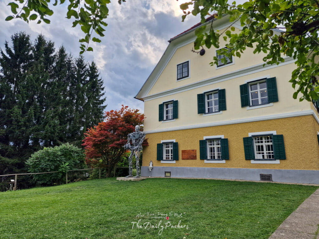 Back garden of the Arnold Schwarzenegger Museum with visitors walking near the Terminator statue.