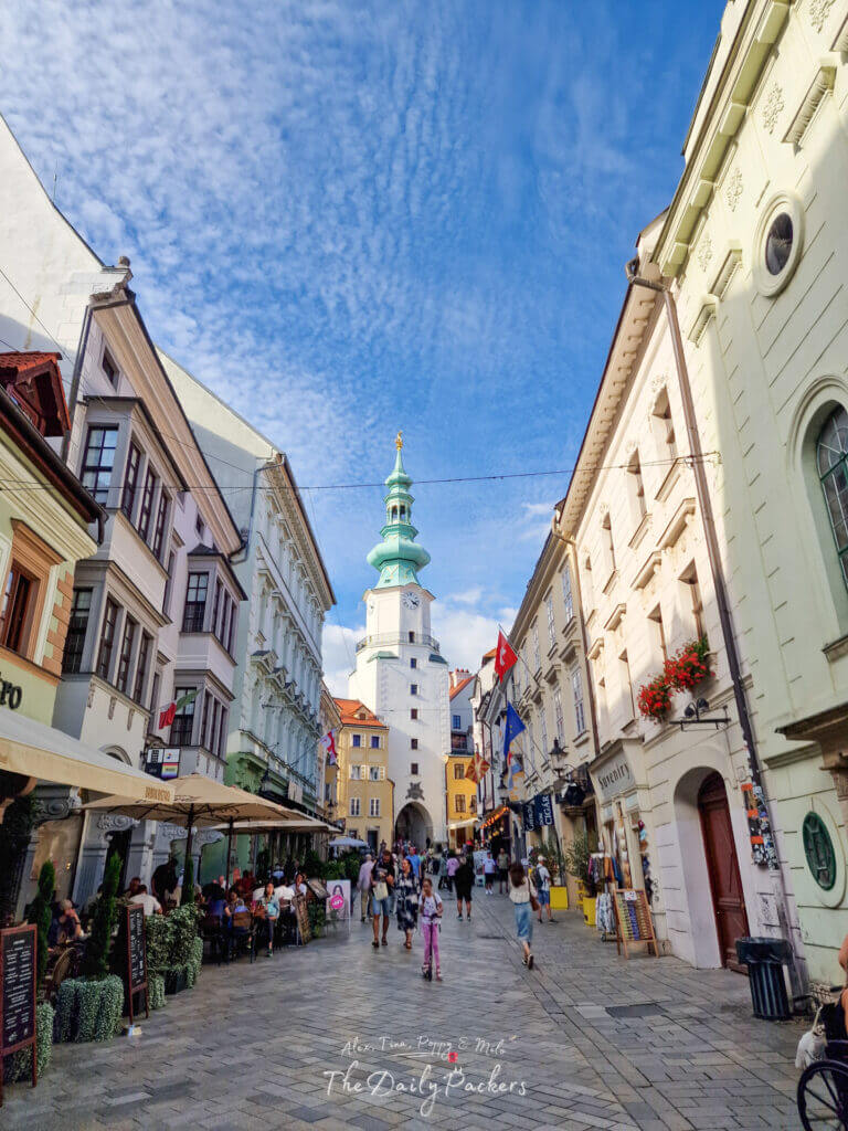 View of Michael’s Gate with its green spire, surrounded by historic buildings and outdoor cafés in Bratislava Old Town.
