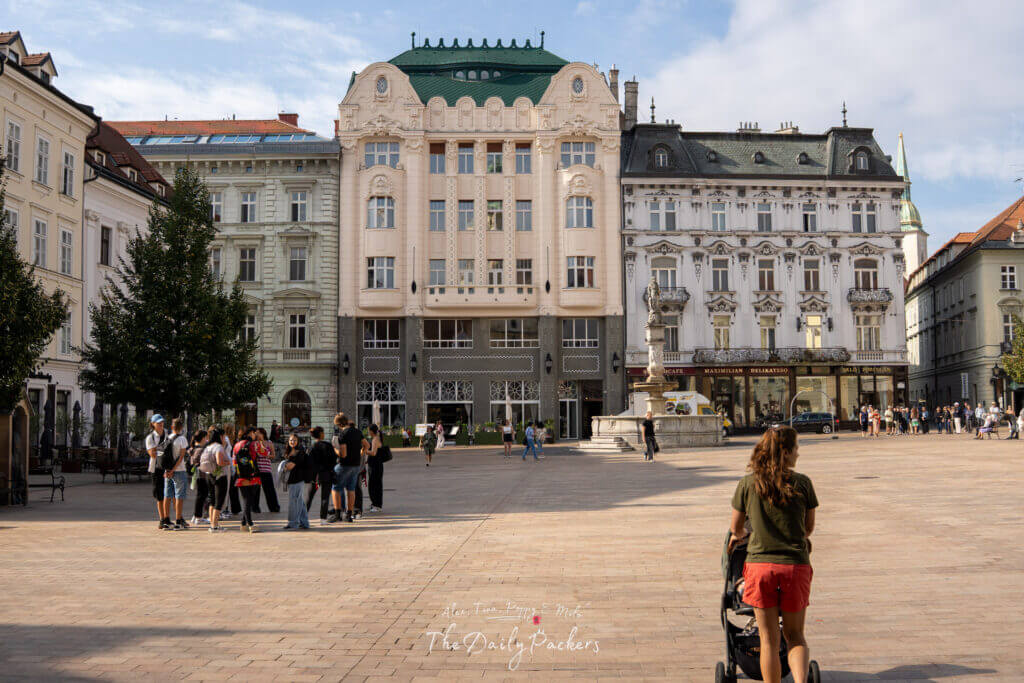 View of Bratislava’s Main Square with art nouveau and baroque buildings and people walking in the plaza.