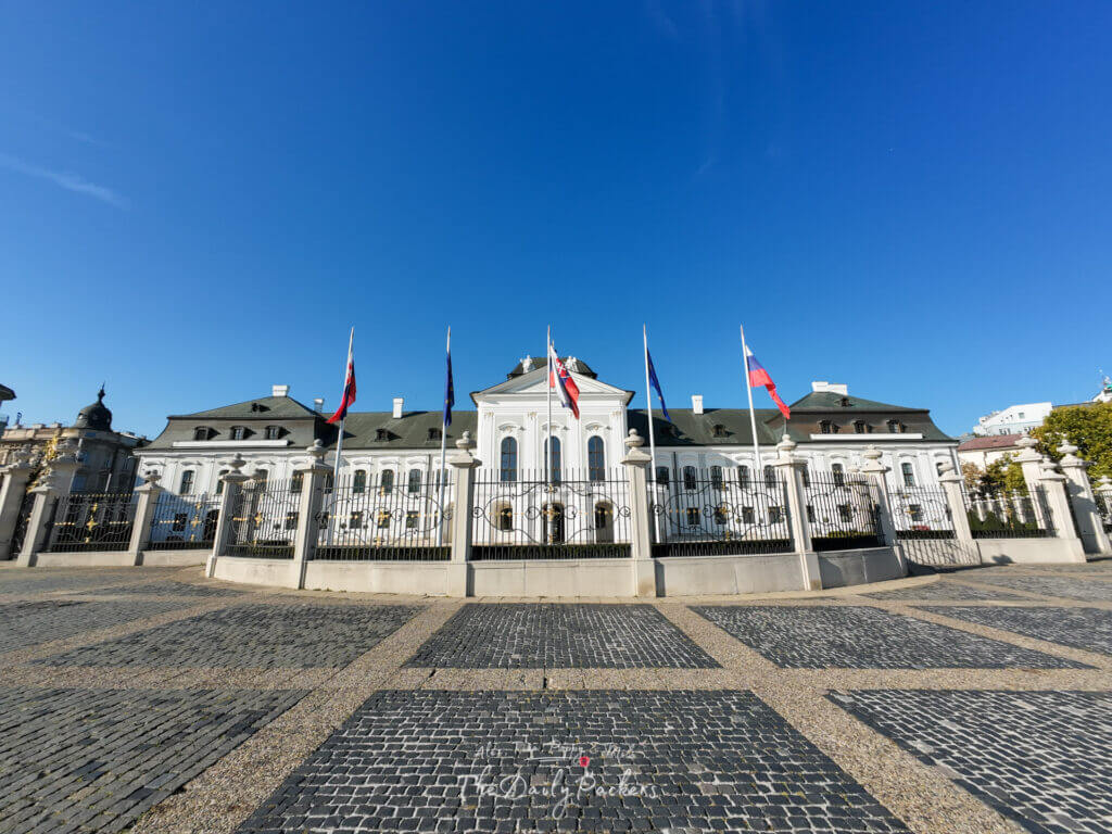 Exterior view of Bratislava Presidential Palace with Slovak and EU flags in front under a clear blue sky
