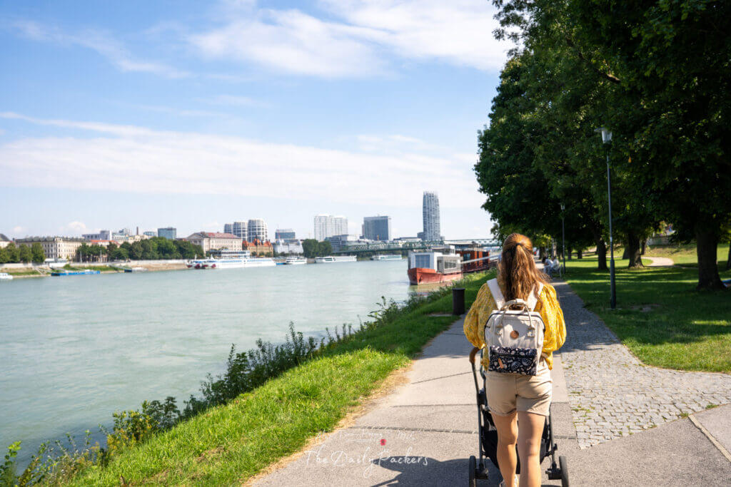 Woman pushing a stroller along the Danube promenade in Bratislava with city views ahead