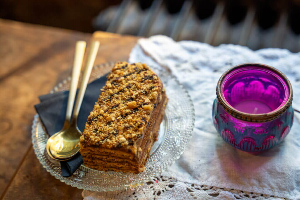 Slice of traditional Slovak layered cake with nuts served on a glass plate with golden cutlery and a purple candle.