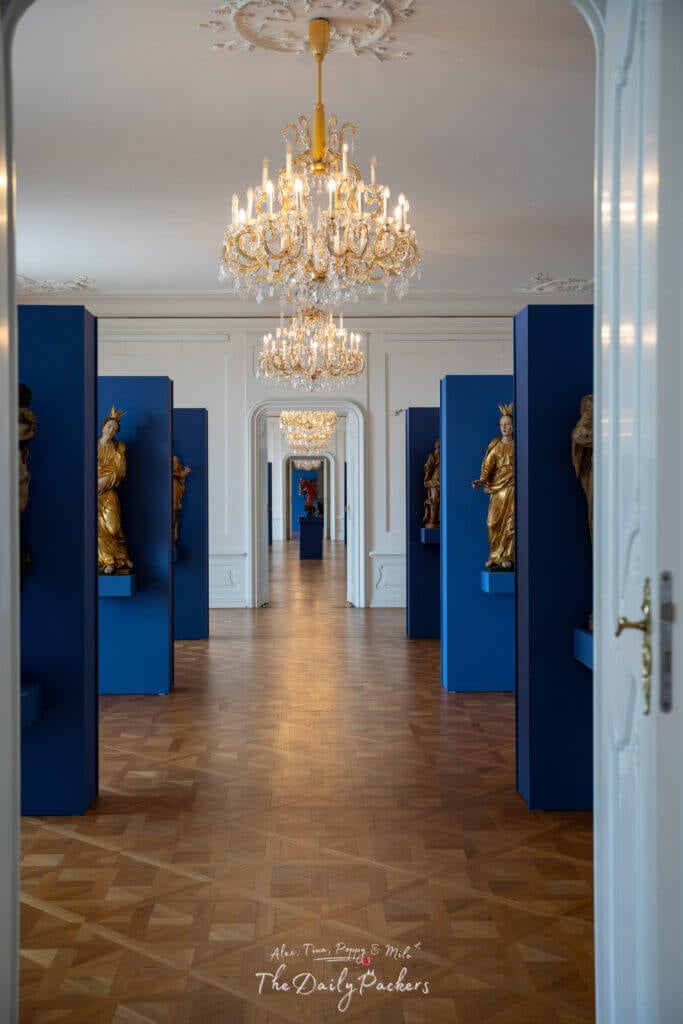 Elegant chandelier-lit hall lined with statues and parquet flooring inside Bratislava Castle museum.