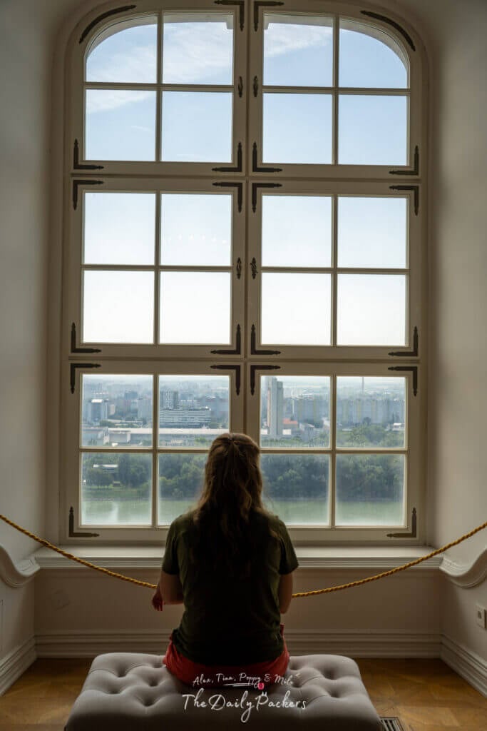 Woman sitting by a tall window overlooking the Danube River and Bratislava city skyline from the castle.