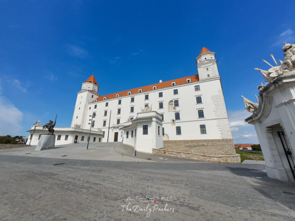 Wide-angle view of Bratislava Castle with its white facade, towers, and blue sky background.