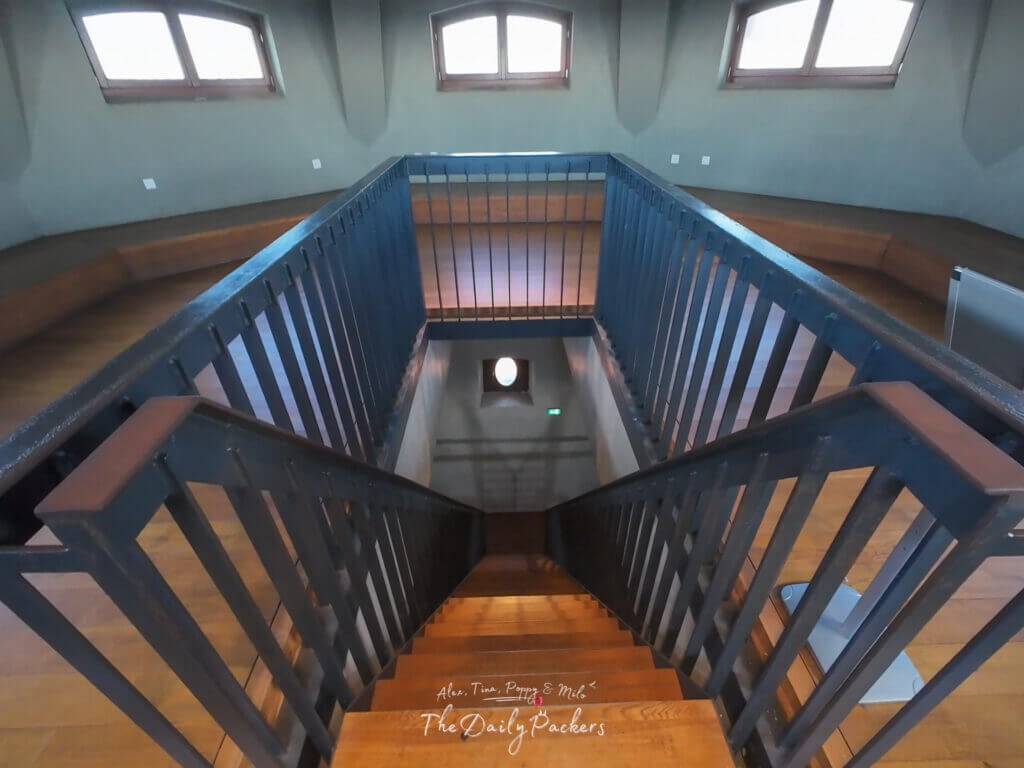 Wooden staircase inside a Bratislava Castle tower with railings and arched windows.