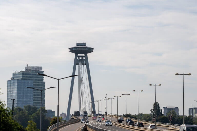 Bratislava UFO Tower standing tall above the SNP Bridge with cars driving toward the observation deck.