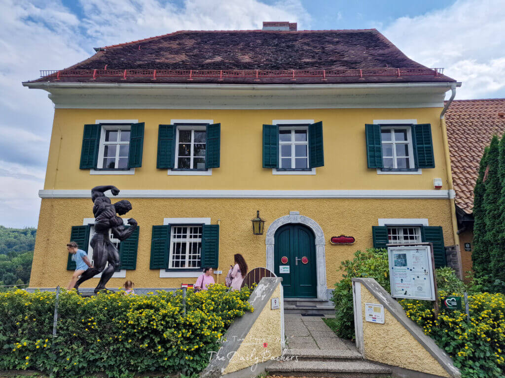 Vue de face du musée Arnold Schwarzenegger à Thal avec une statue de bronze de Schwarzenegger en train de poser devant.