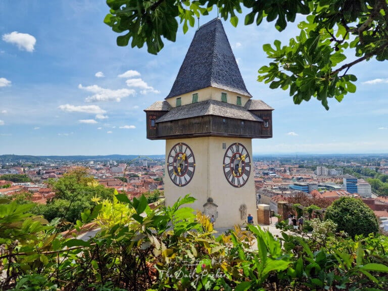 The iconic Uhrturm clock tower seen from the Old Town of Graz with baroque façades in the foreground.