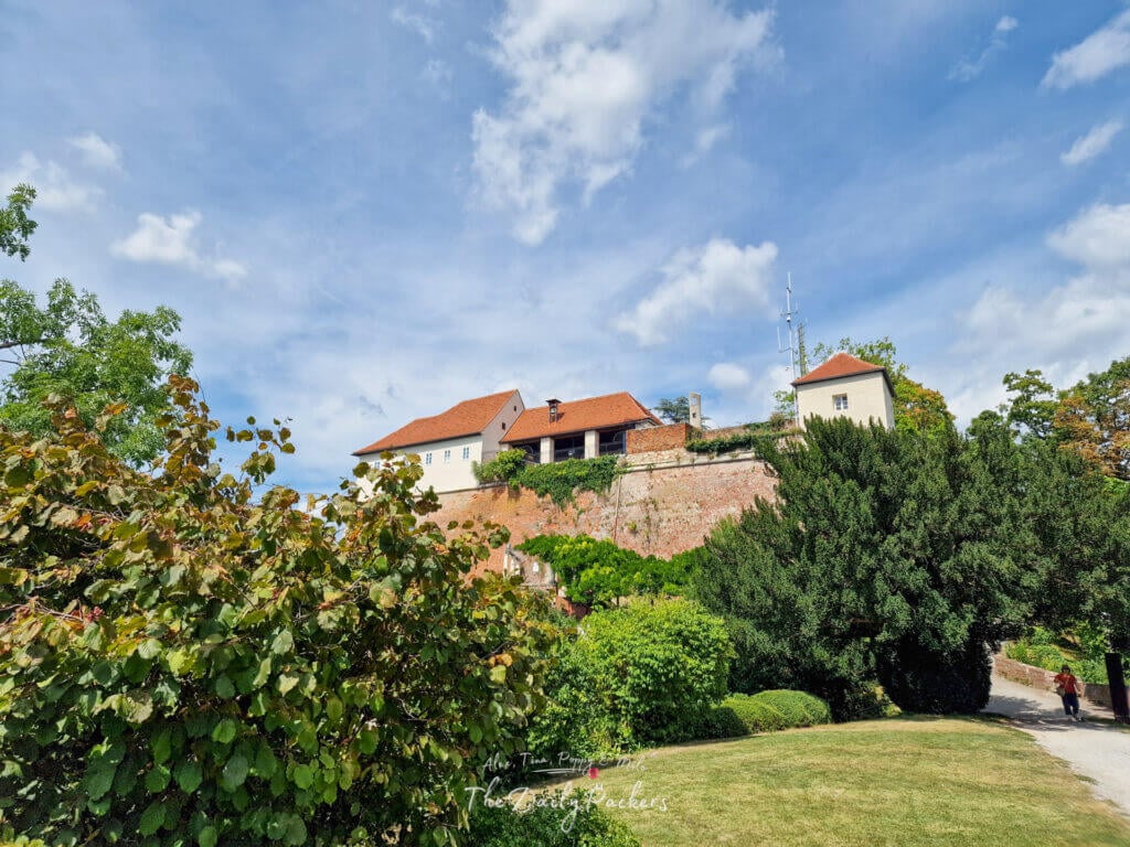 Vue des murs fortifiés et des bâtiments sur le Schlossberg de Graz entourés de verdure.
