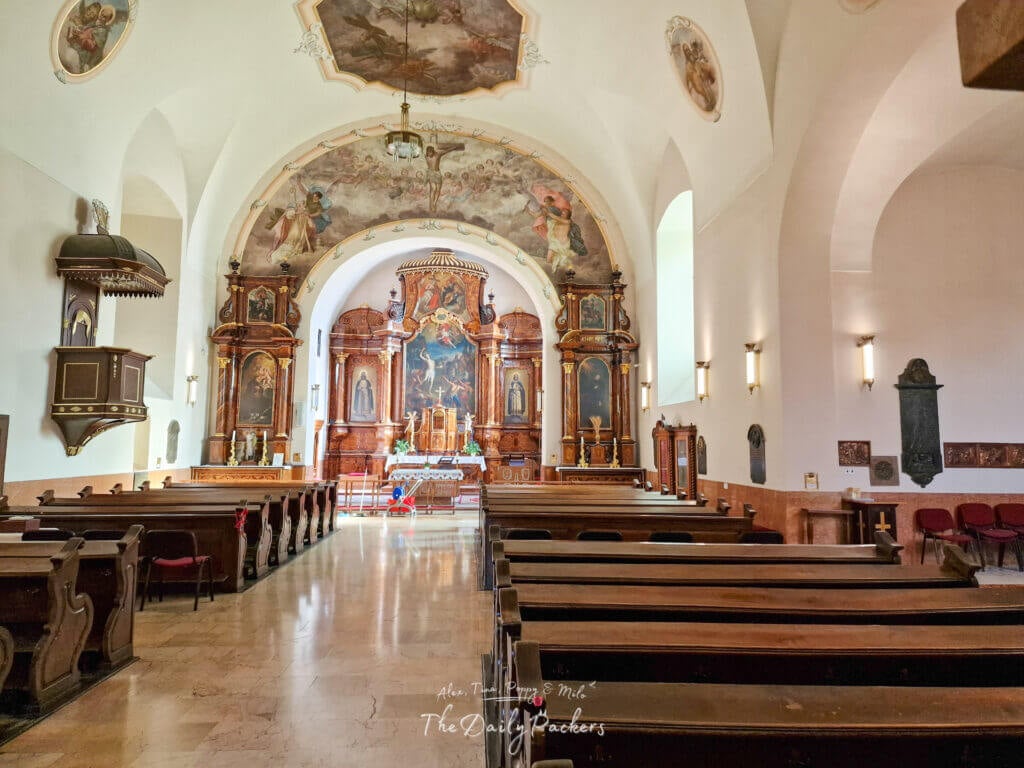 Interior of Saint Sebastian Church in Pécs, showing ornate wooden pews, altars, and frescoes decorating the ceiling.