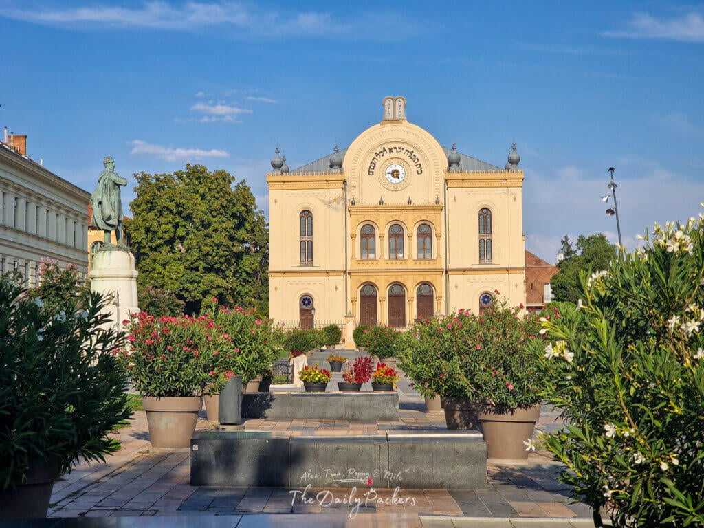 Close-up view of the Pécs Synagogue with its yellow facade, Hebrew inscription, and clock above the main entrance.