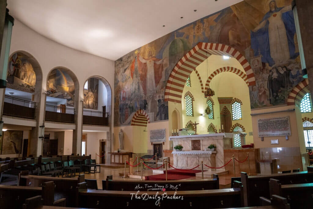 Interior of the Church of the Blessed Virgin Mary in Pécs with a crucifix, arched windows, and the decorated dome.