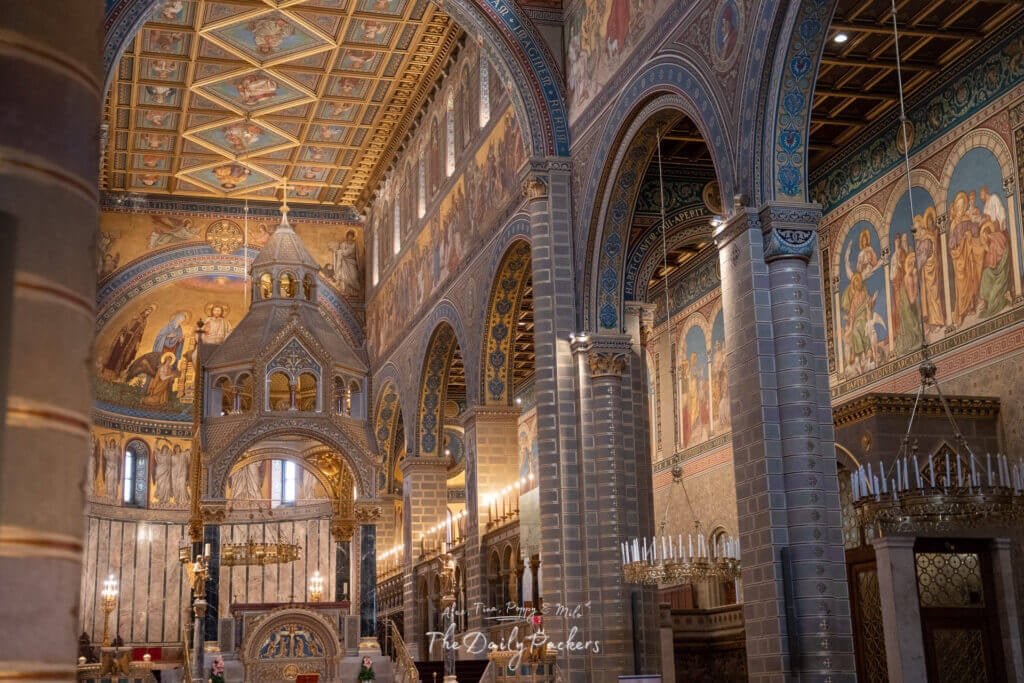 Interior of Pécs Cathedral showcasing its detailed murals, arches, and candle-lit chandeliers.