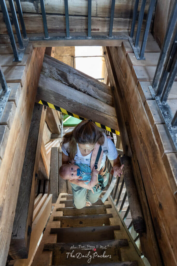 A woman carrying a baby climbs the wooden stairs inside the tower of Pécs Cathedral.