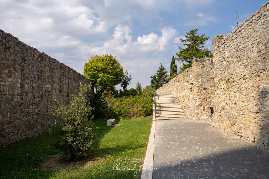 Path along the northern castle wall in Pécs with stone walls, green grass, and trees on a sunny day