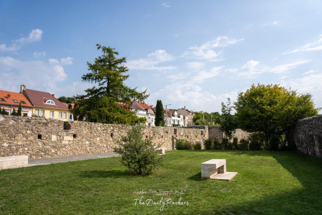 View of the northern castle wall in Pécs with grassy areas, trees, and colorful houses in the background