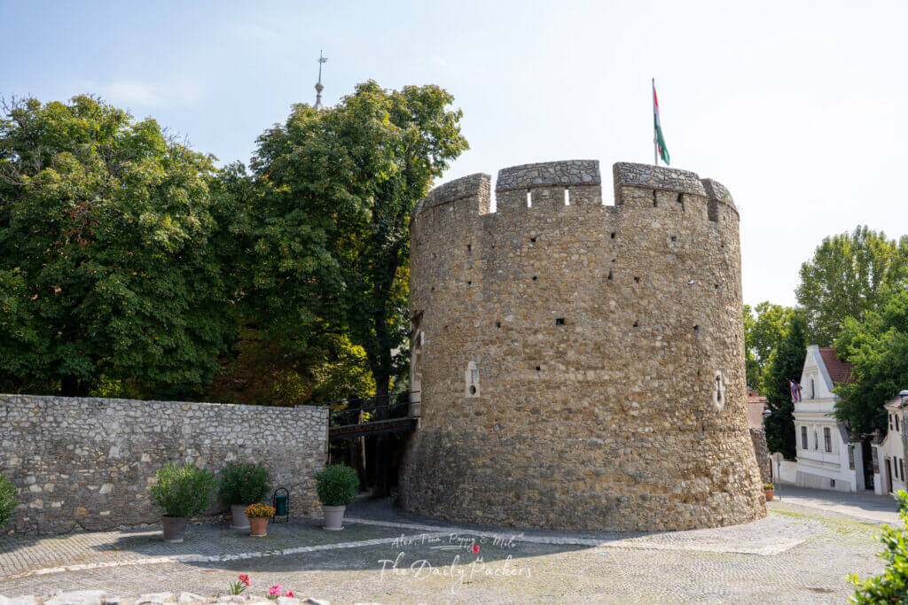 Exterior of the Barbican in Pécs, a round stone tower with an archway and Hungarian flag on top