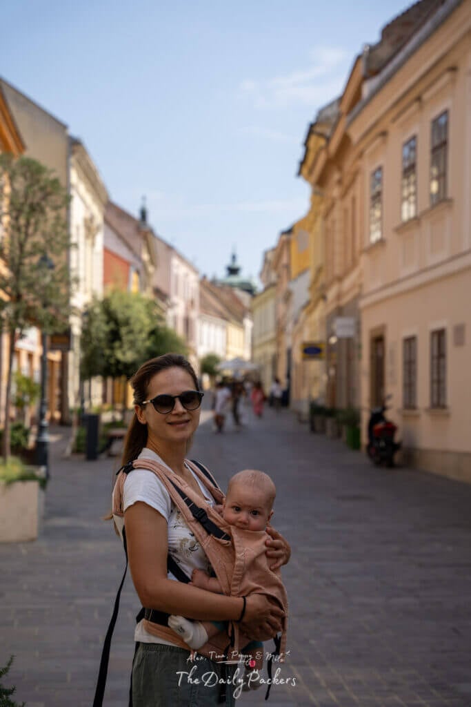 Mother carrying her baby in a carrier while strolling through the picturesque streets of Pécs old town.
