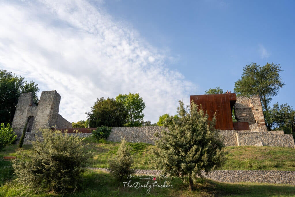 Ruins of the old Tettye building in Pécs, surrounded by greenery and stone walls under a partly cloudy sky
