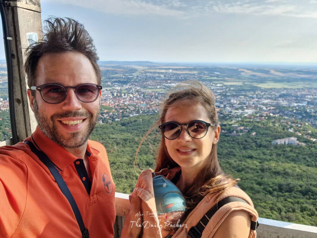 Couple taking a selfie with their baby at the Pécs TV tower viewpoint, overlooking the city below