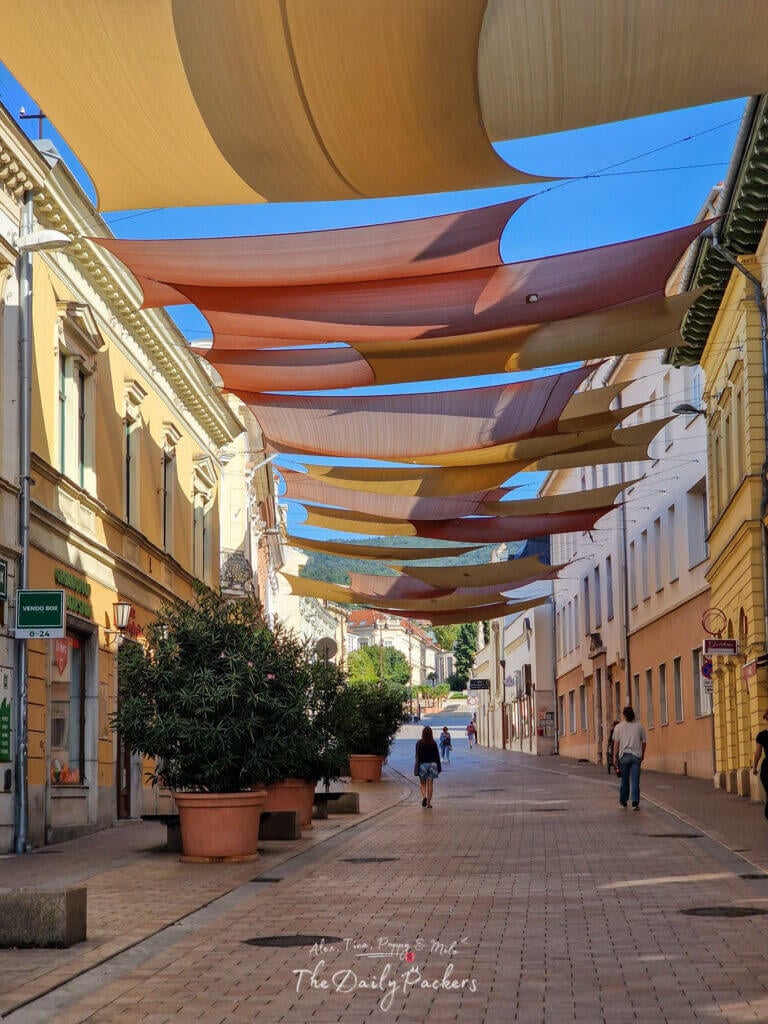 Irgalmasok Street in Pécs with colorful hanging shades and people walking through the historic old town
