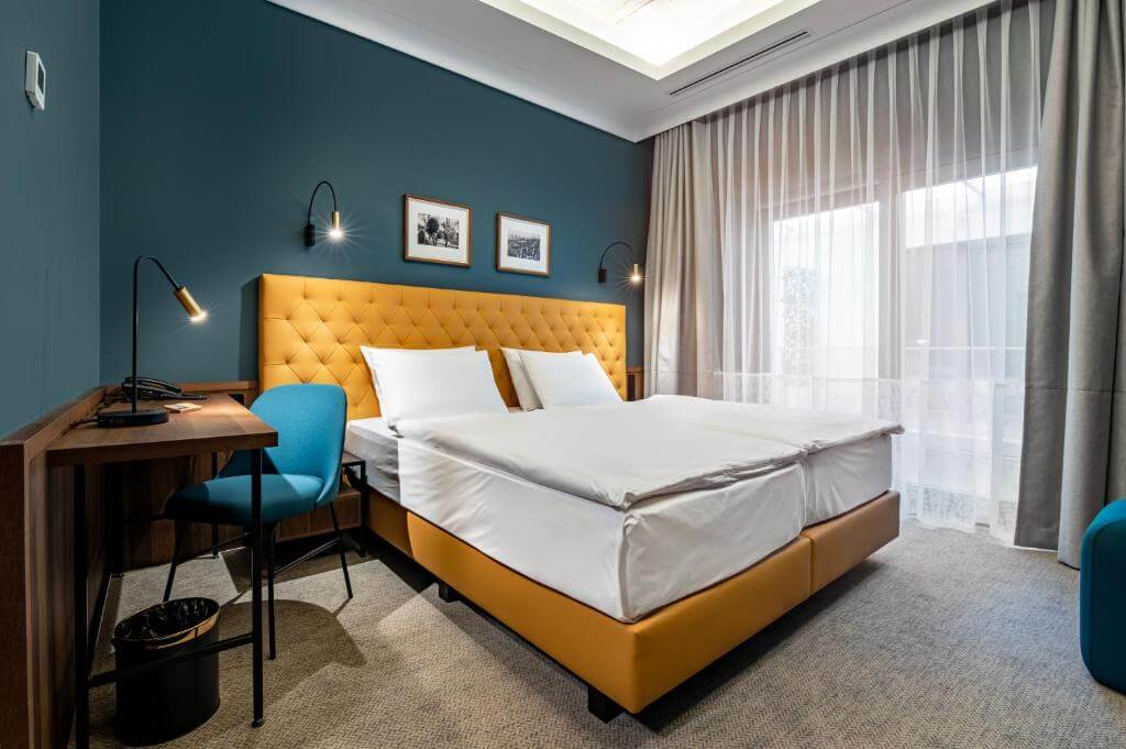 Modern double room at Palatinus Boutique Hotel in Pécs with a mustard-yellow headboard and minimalist design.