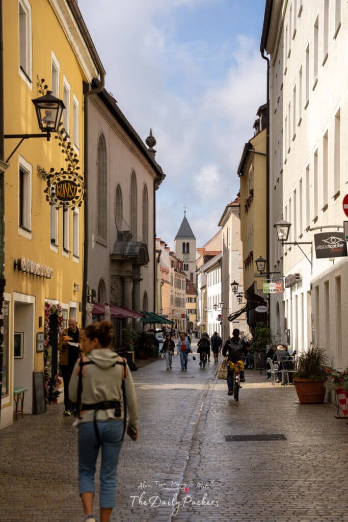 Street view of Regensburg city center with colorful houses, cafes, and people walking on the cobblestone lane.