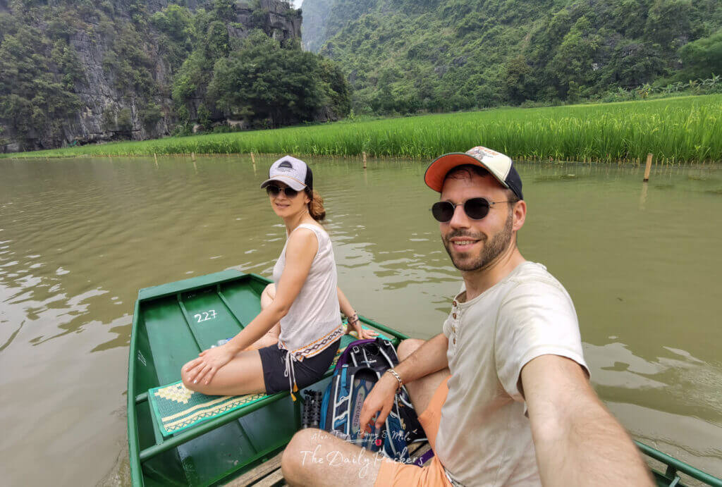 Couple taking a selfie while on a rowboat, surrounded by green rice fields and limestone cliffs.