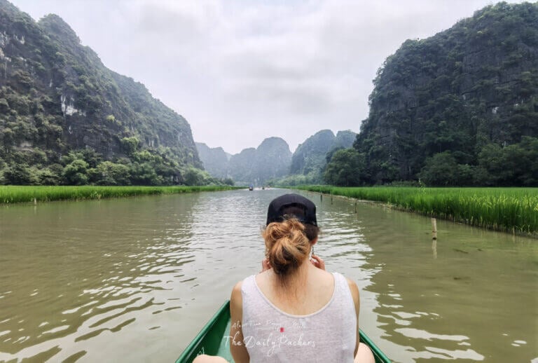 Tourist sitting on a rowboat, enjoying the peaceful scenery of rice fields and mountains in Tam Coc.