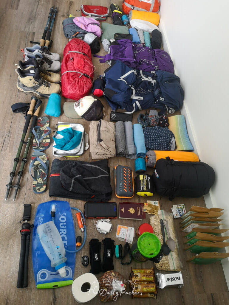 Detailed flat lay of hiking equipment including food rations, hydration packs, camping gear, footwear, and technical clothing for Tour du Mont Blanc