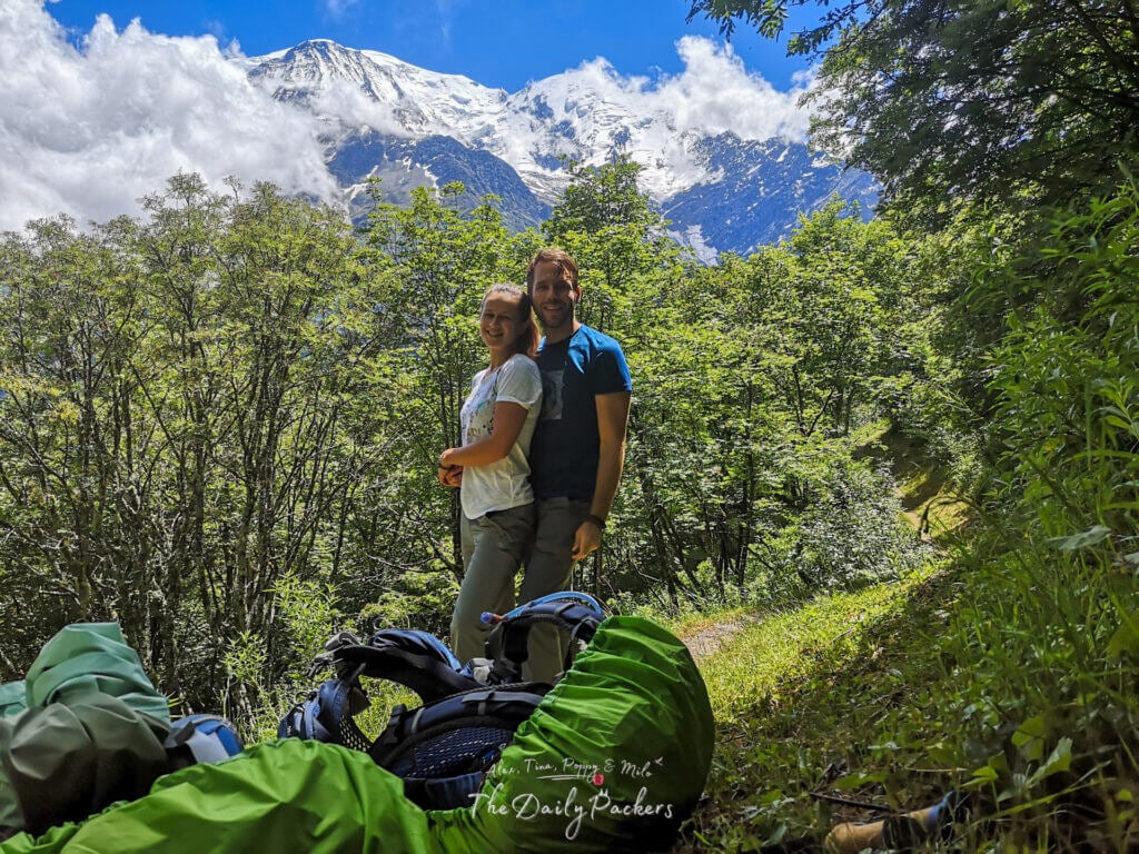 Couple of hikers posing on a forest trail with Mont Blanc’s snow-capped peaks in the background.