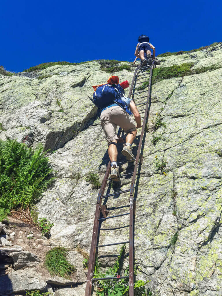 Climbers ascending a vertical iron ladder under cloudless skies