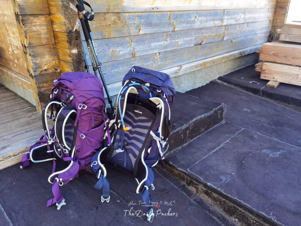 Our two backpacks and trekking poles resting against a weathered wall.