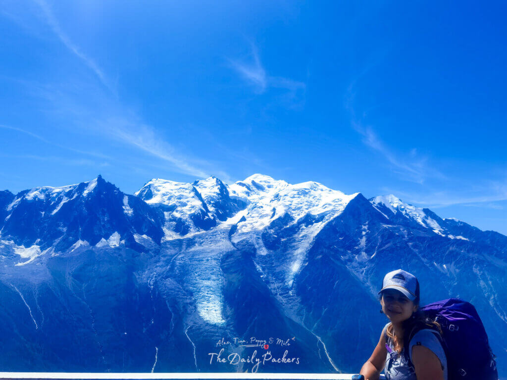 At Brévent viewpoint—woman with purple pack smiling toward Mont Blanc.